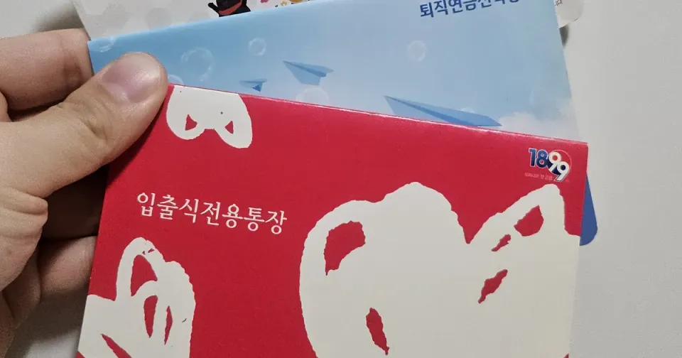 Three Korean bank passbooks held in one hand, the top one a Woori Bank deposit passbook