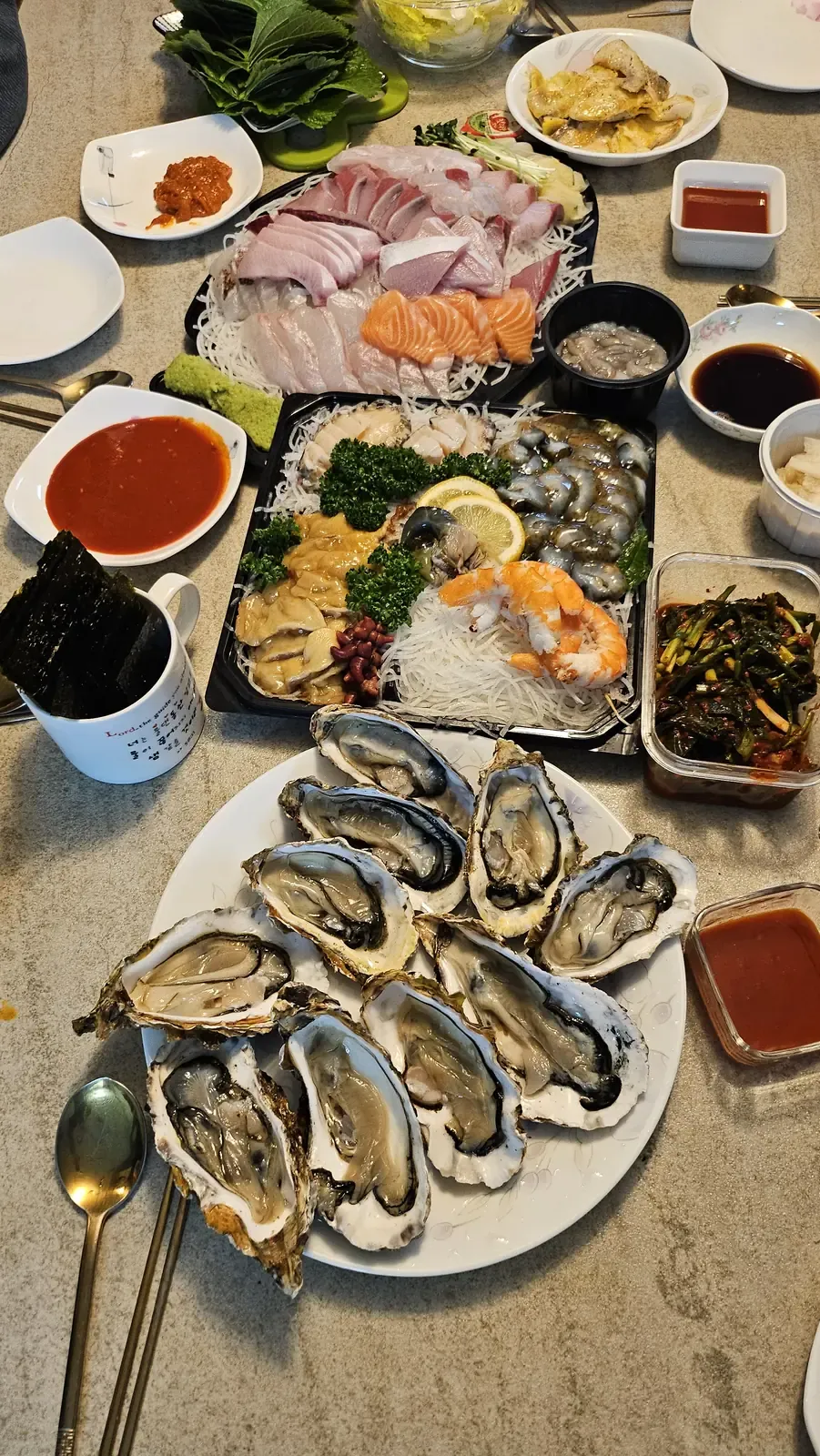 An overhead view of a market table with a sashimi platter, oysters, side dishes and dipping sauces