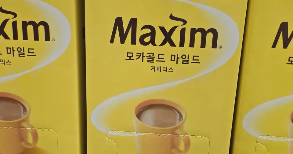Yellow boxes of Maxim Mocha Gold Mild coffee mix stacked on a Korean supermarket shelf