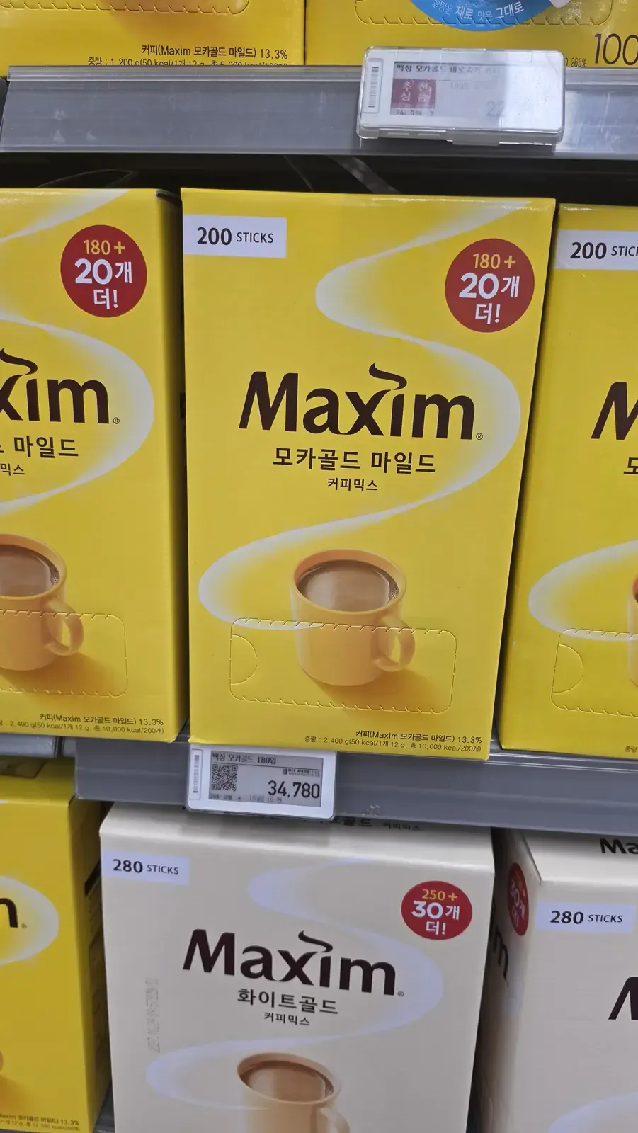 Yellow boxes of Maxim Mocha Gold Mild coffee mix on a supermarket shelf with an electronic price label reading 34,780 won