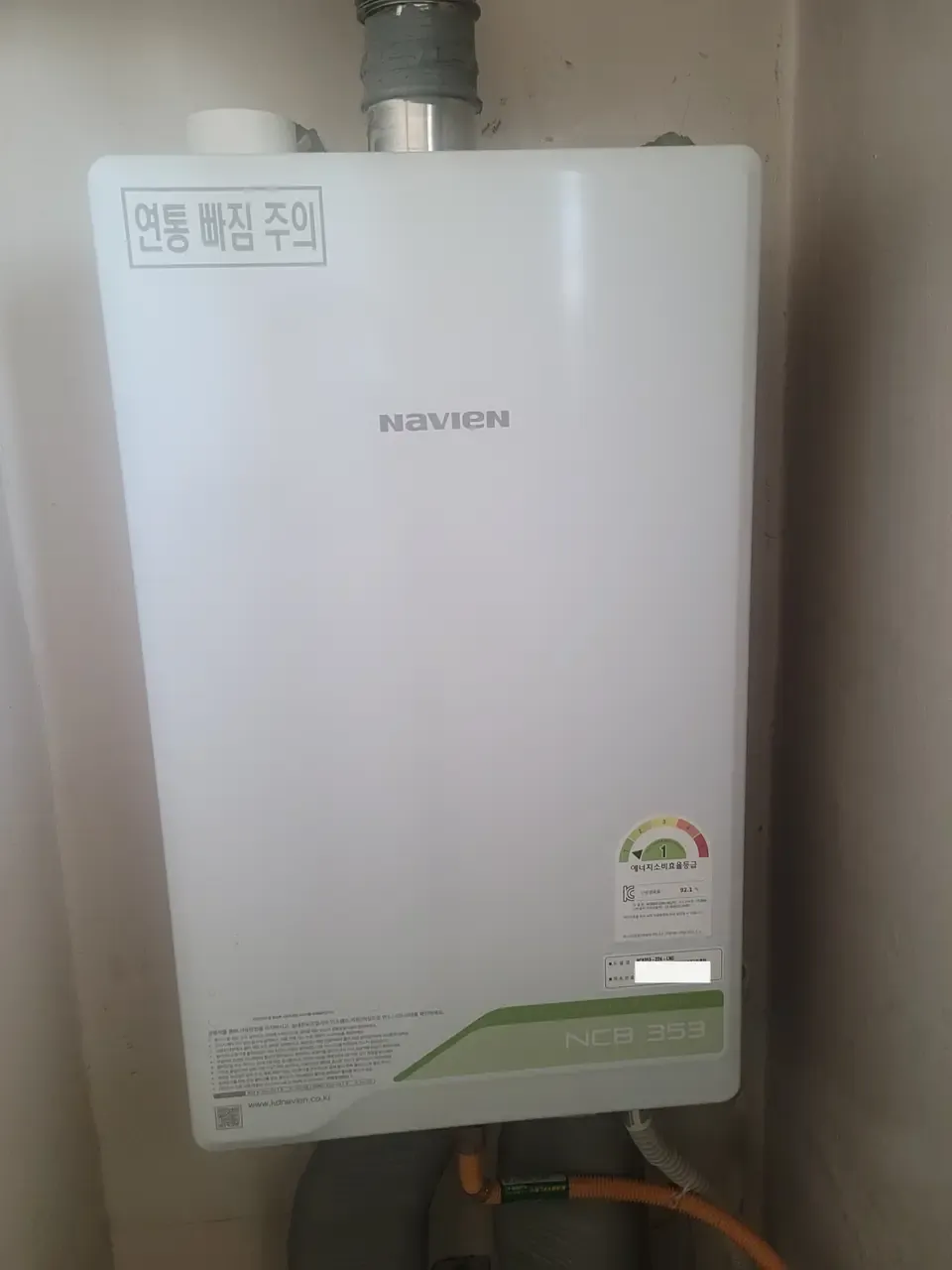 A wall-mounted Navien NCB353 condensing boiler installed in a utility recess, flue pipe above and gas line to the side