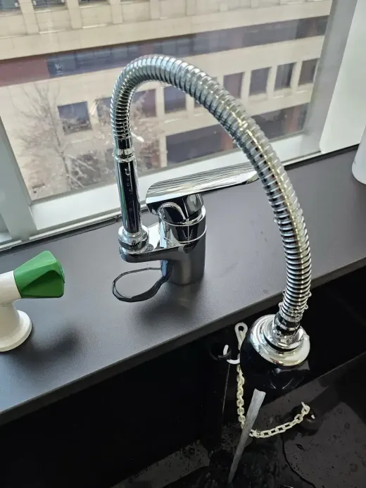 A newly installed kitchen faucet with a flexible hose on a black sink