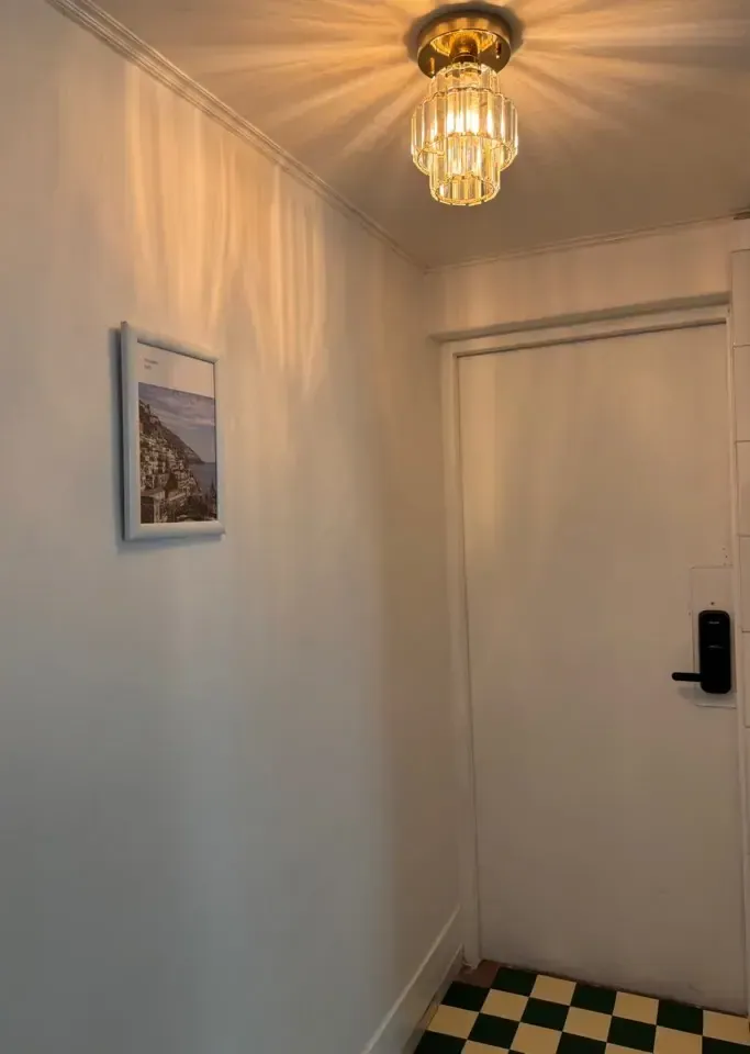 A hallway with a tall lockable personal storage cabinet under a small chandelier