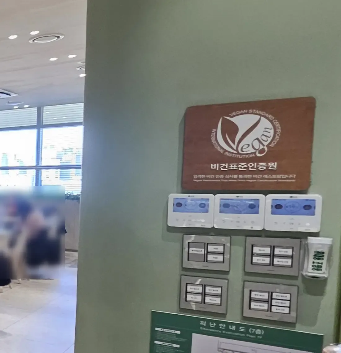 A wooden plaque on a green wall reading Vegan Standard Certification, International Institution, ๋น๊ฑดํ์ค์ธ์ฆ์