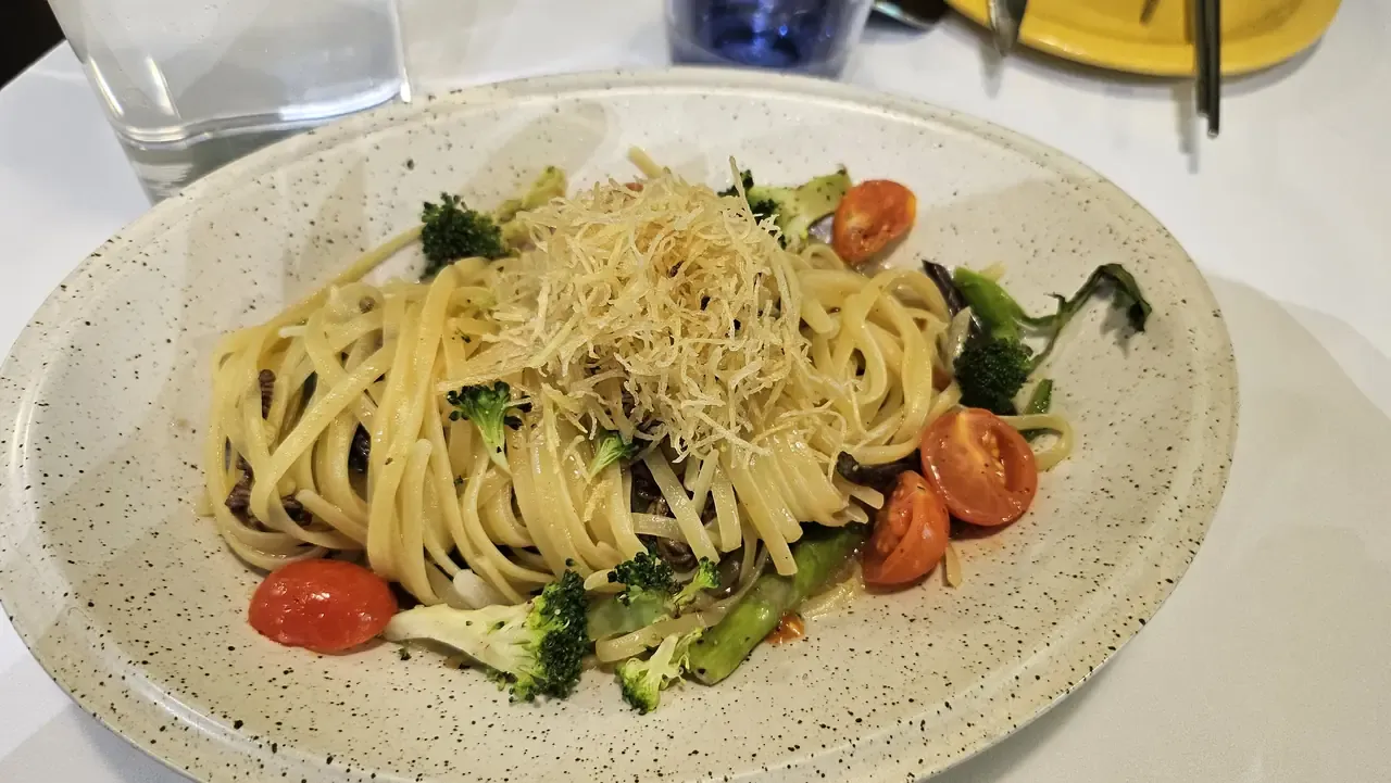 A plate of linguine with broccoli, cherry tomatoes and crisp shredded topping