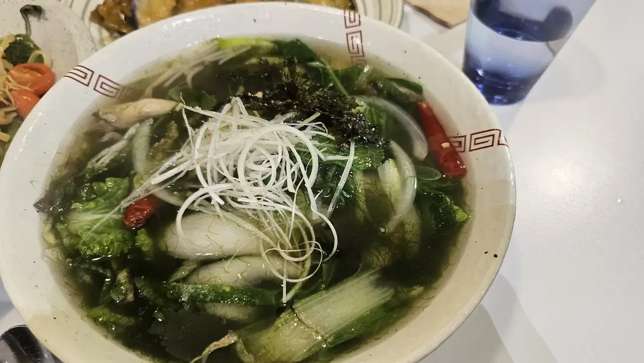 A bowl of clear seaweed rice noodle soup with greens, spring onion and dried chilli