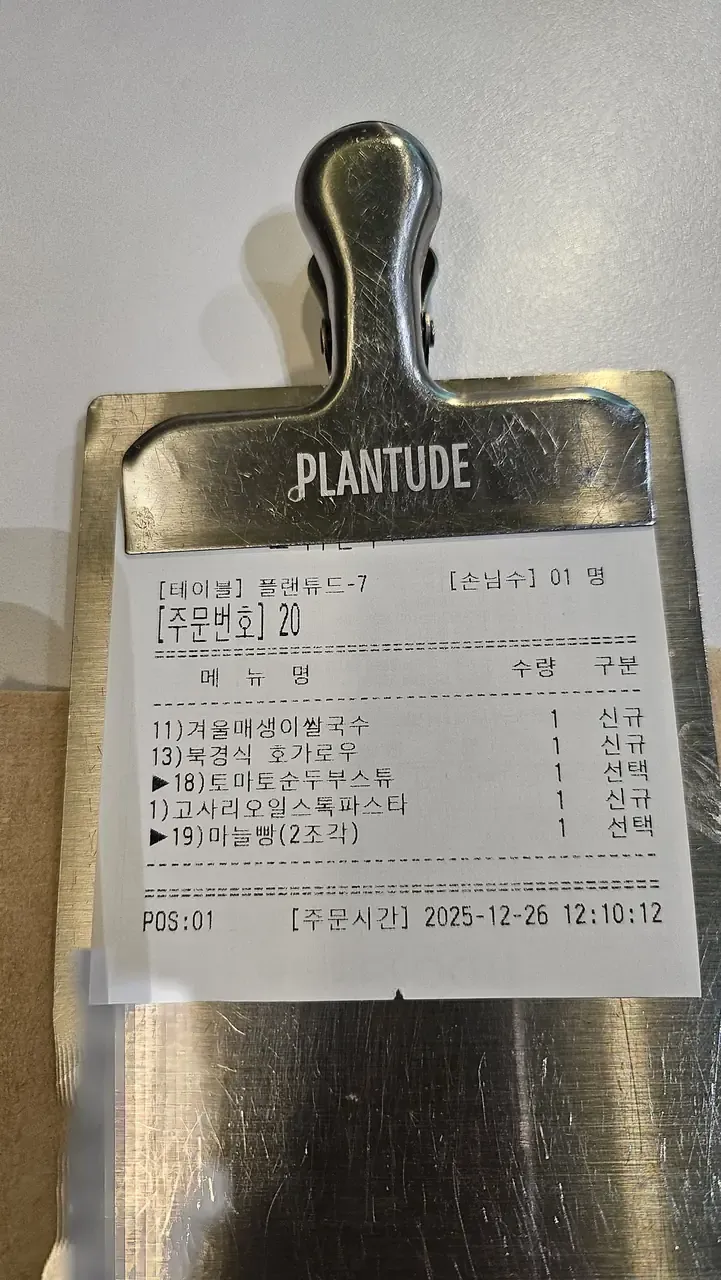A restaurant order slip clipped to a metal board, listing five Korean menu items