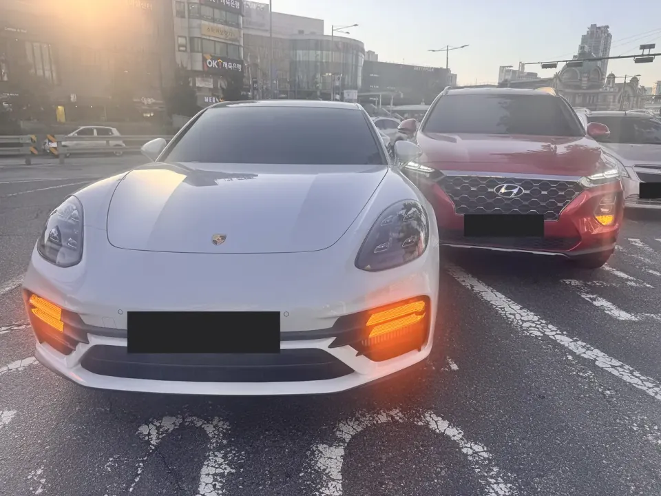 A white Porsche and a red SUV stopped in a Seoul junction with hazard lights on after a minor collision, licence plates obscured