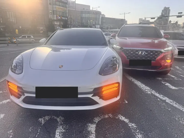 A white Porsche and a red SUV stopped in a Seoul junction with hazard lights on after a minor collision, licence plates obscured