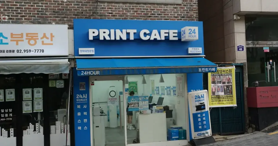 A blue shop sign reading PRINT CAFE 24 above a Seoul storefront with copiers visible inside