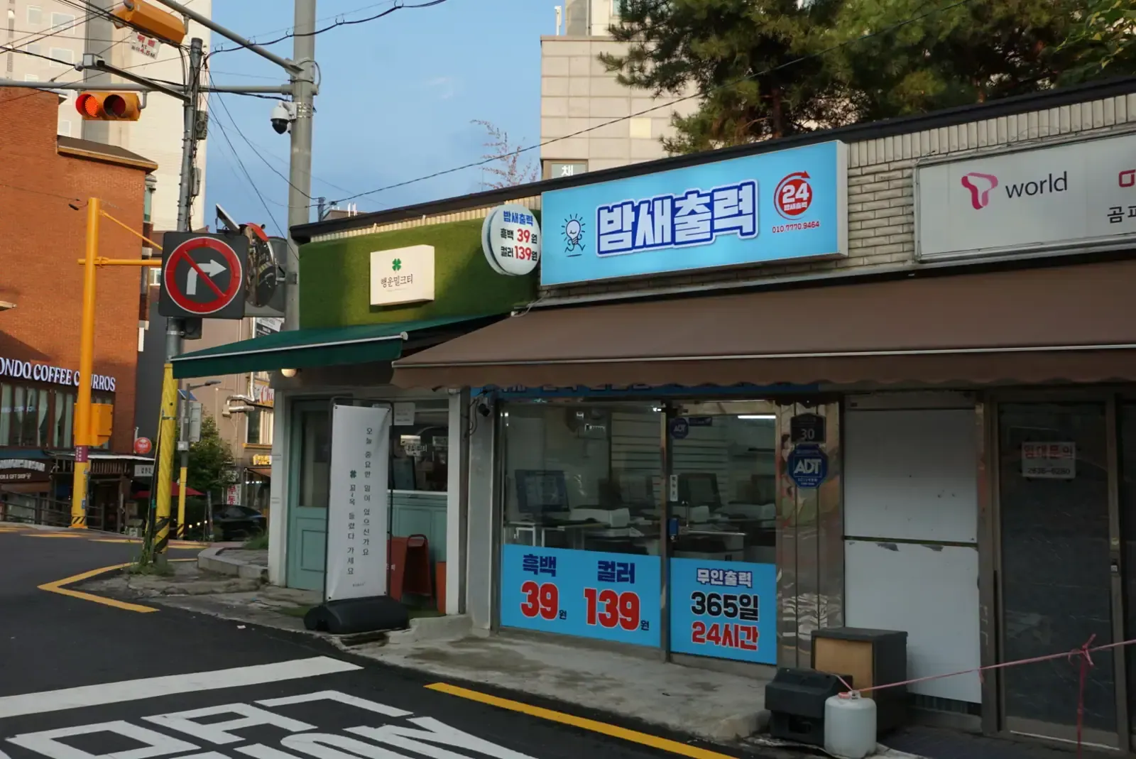 A 24-hour print shop storefront with a sign advertising black and white printing at 39 won and colour at 139 won, open 365 days
