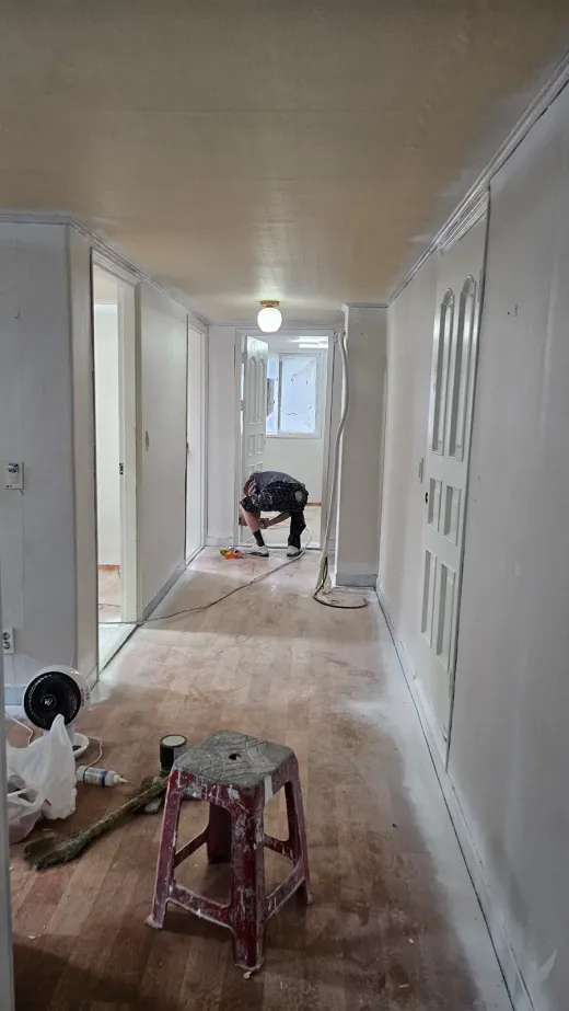 A coliving house corridor mid-renovation, floors stripped back and doors off, with tools on the ground