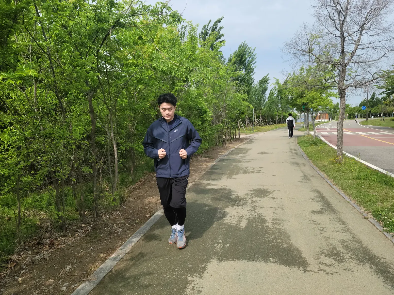 A runner on a paved park path in Seoul, with a separate red-surfaced bike lane and a road running alongside