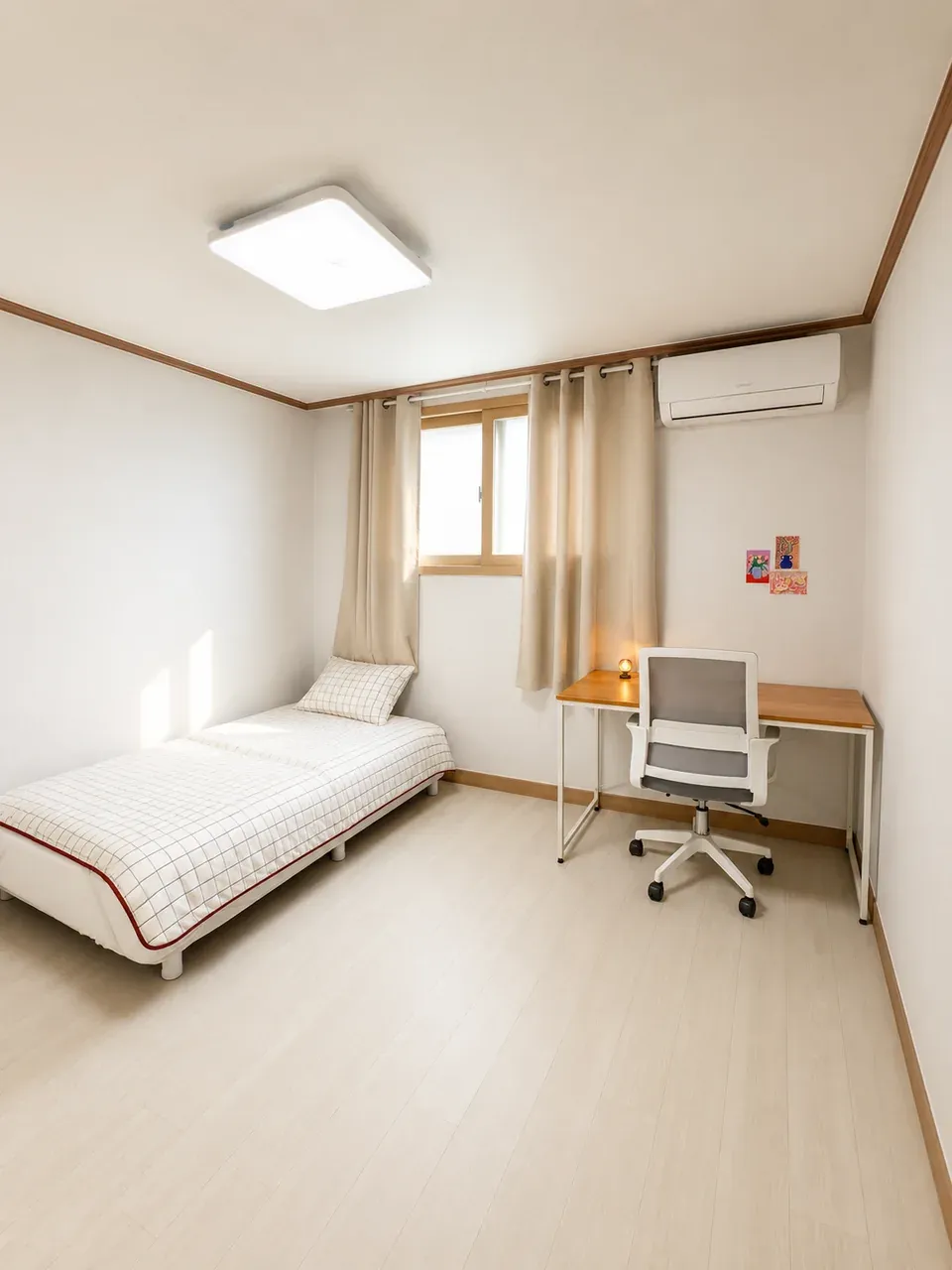 A single room with the bed on the left under the window, the desk and chair along the right-hand wall and the air conditioner above it