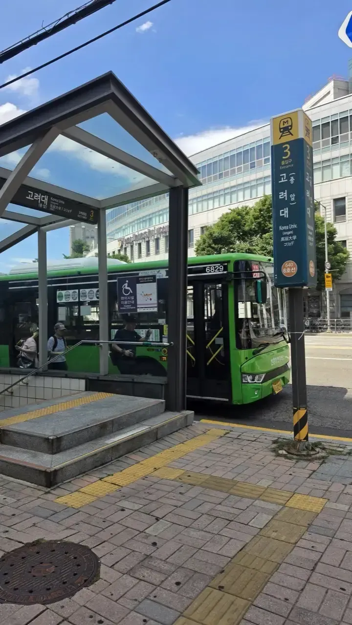 A green Seoul city bus at a covered bus stop in daylight