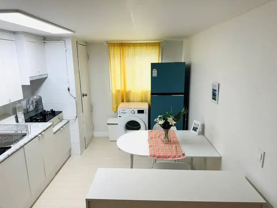 A shared kitchen with white cabinets, a sink, a teal fridge, a dining table and a yellow curtain