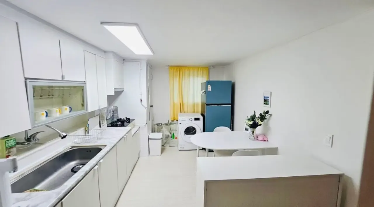 A shared kitchen in a Seoul share house with sink, gas range, washing machine, fridge and a dining table