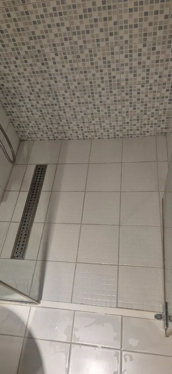 A cleaned shower floor with white tiles, a stainless linear drain and mosaic tiles behind