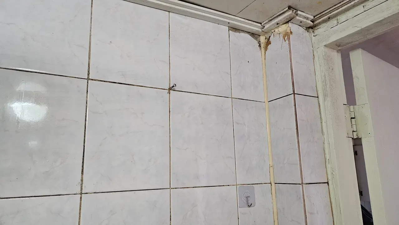 The corner of a bathroom where the silicone seal has gone brown and is running down the tile joint