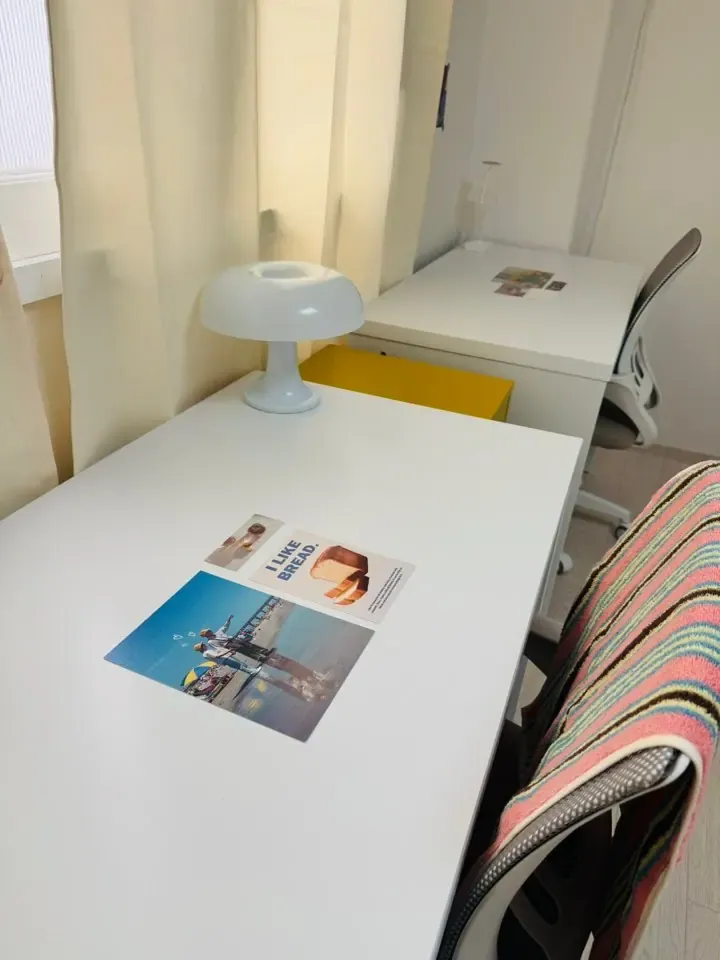 A single room with a desk, lamp and bed under a window