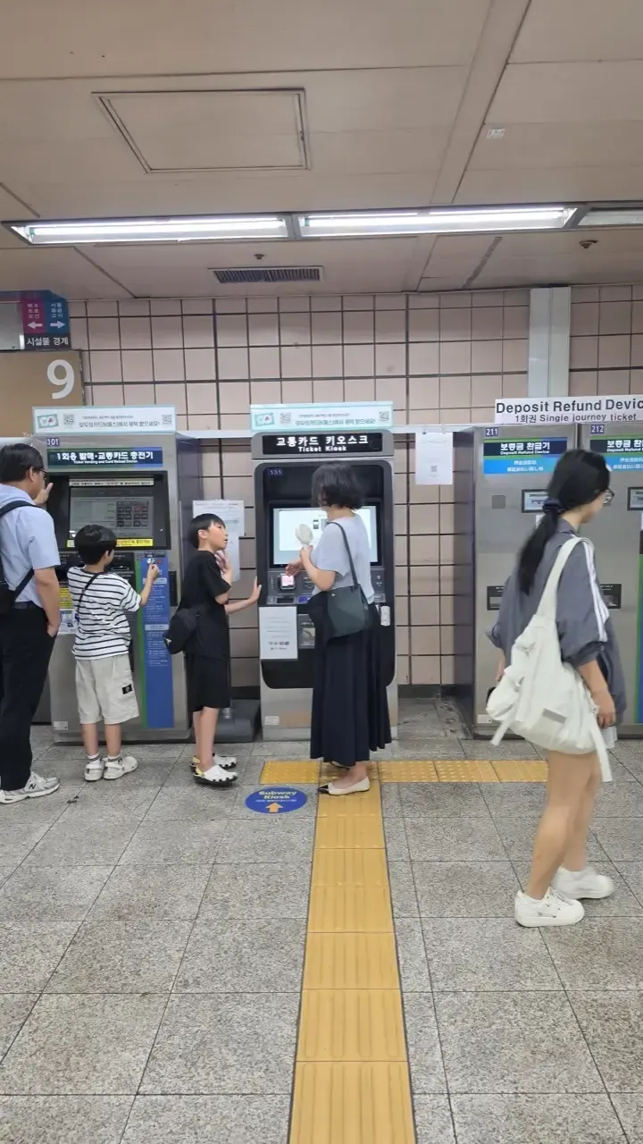 A row of transit card charging kiosks in a Seoul subway station, with a Deposit Refund Device sign in English above them