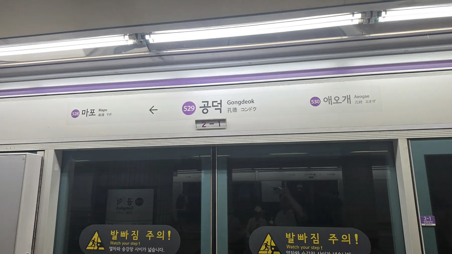 Inside a Seoul subway train, the sign above the doors showing the station Gongdeok and the door number 2-1