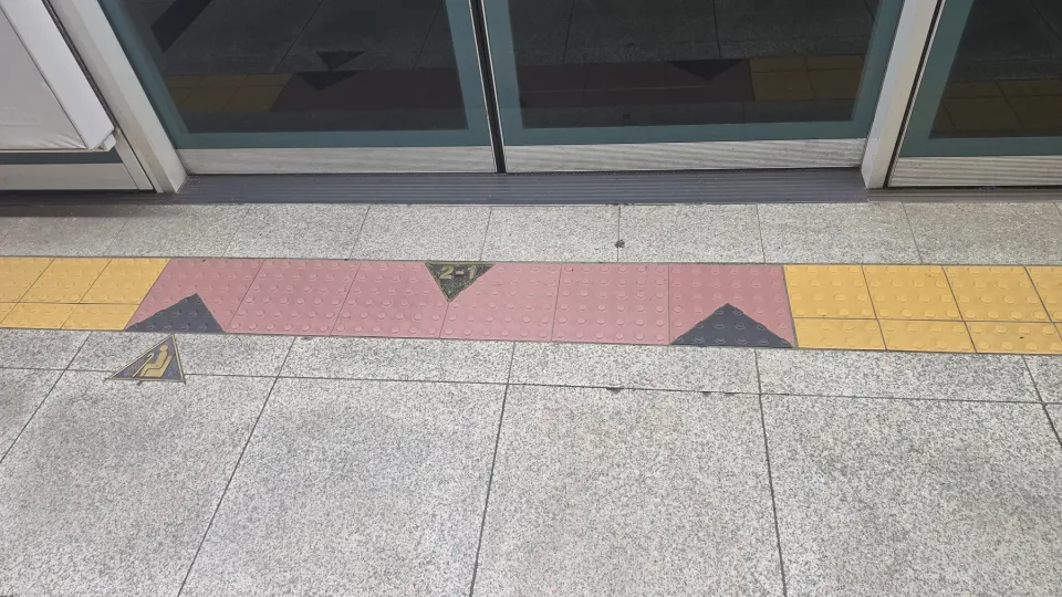 A Seoul subway platform floor marked 2-1 in front of the screen doors, showing the car and door number