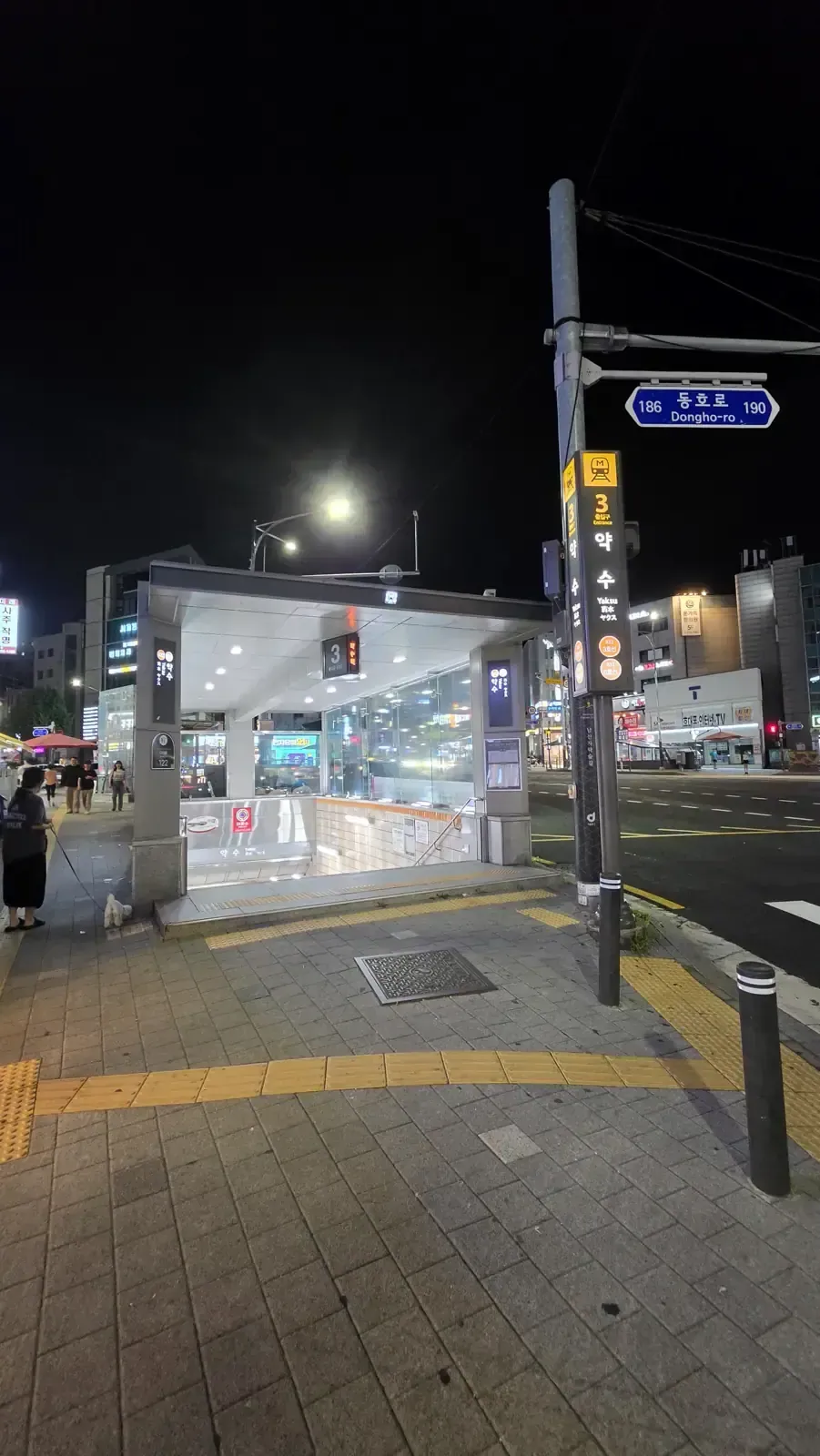 A lit Seoul subway station entrance on a street at night