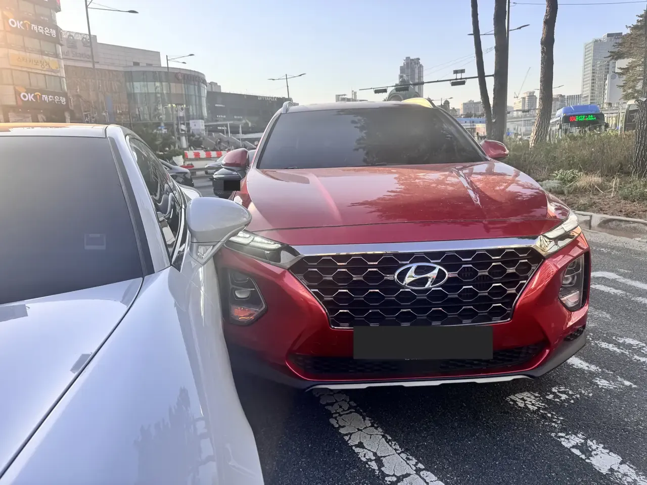 A red SUV's front corner in contact with the side of a white car at a Seoul junction, with Seoul Station buildings behind