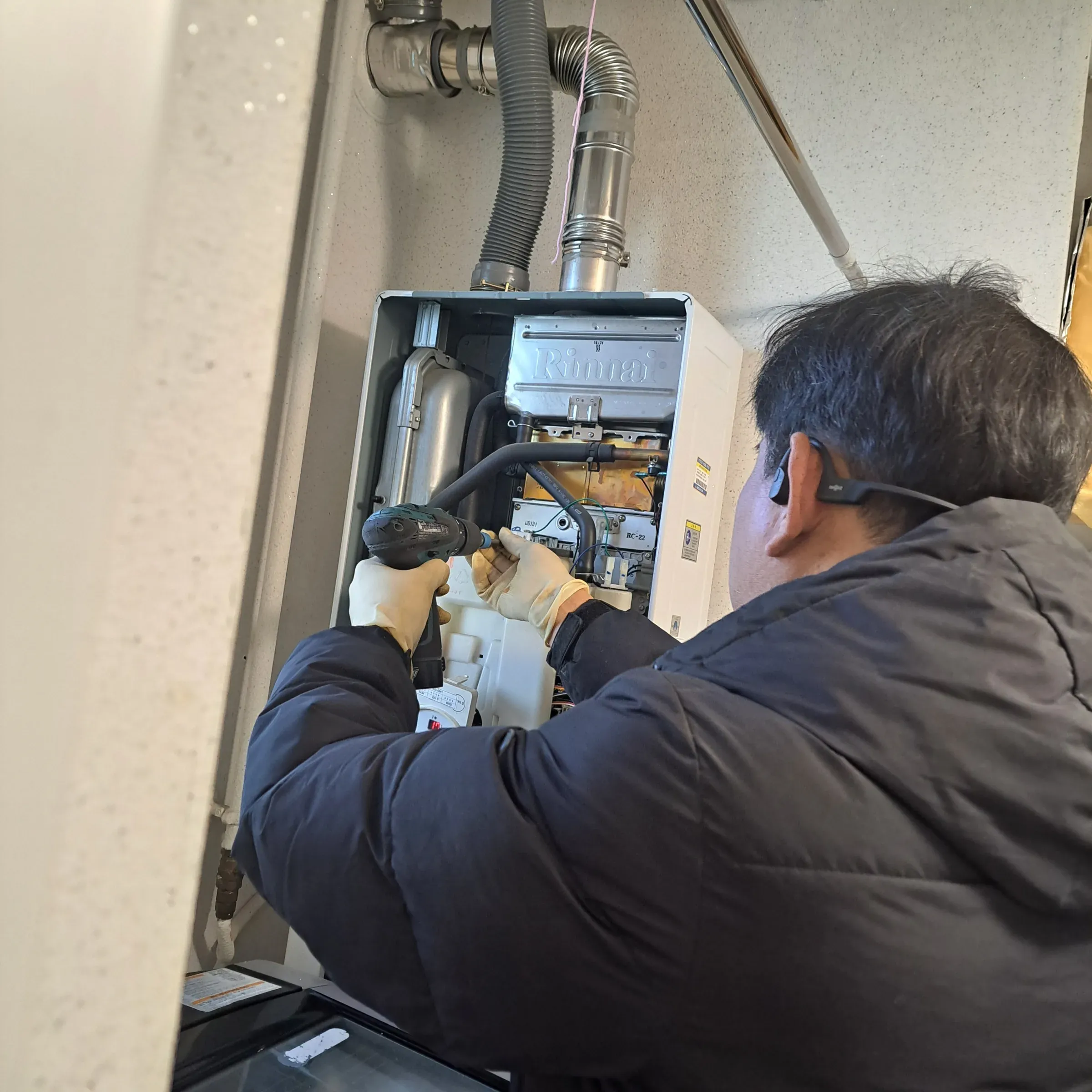 A technician with the boiler cover removed, working on the internal components with a drill