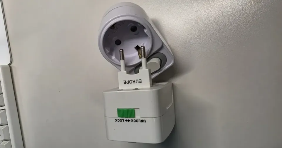 A universal travel adapter with its EUROPE round-pin module slid out, held beside a round Korean wall outlet