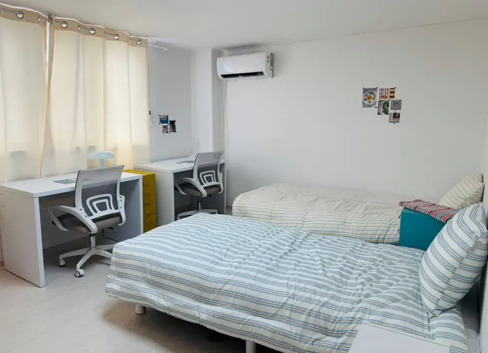 A twin room with two desks, two beds and a wall air conditioner