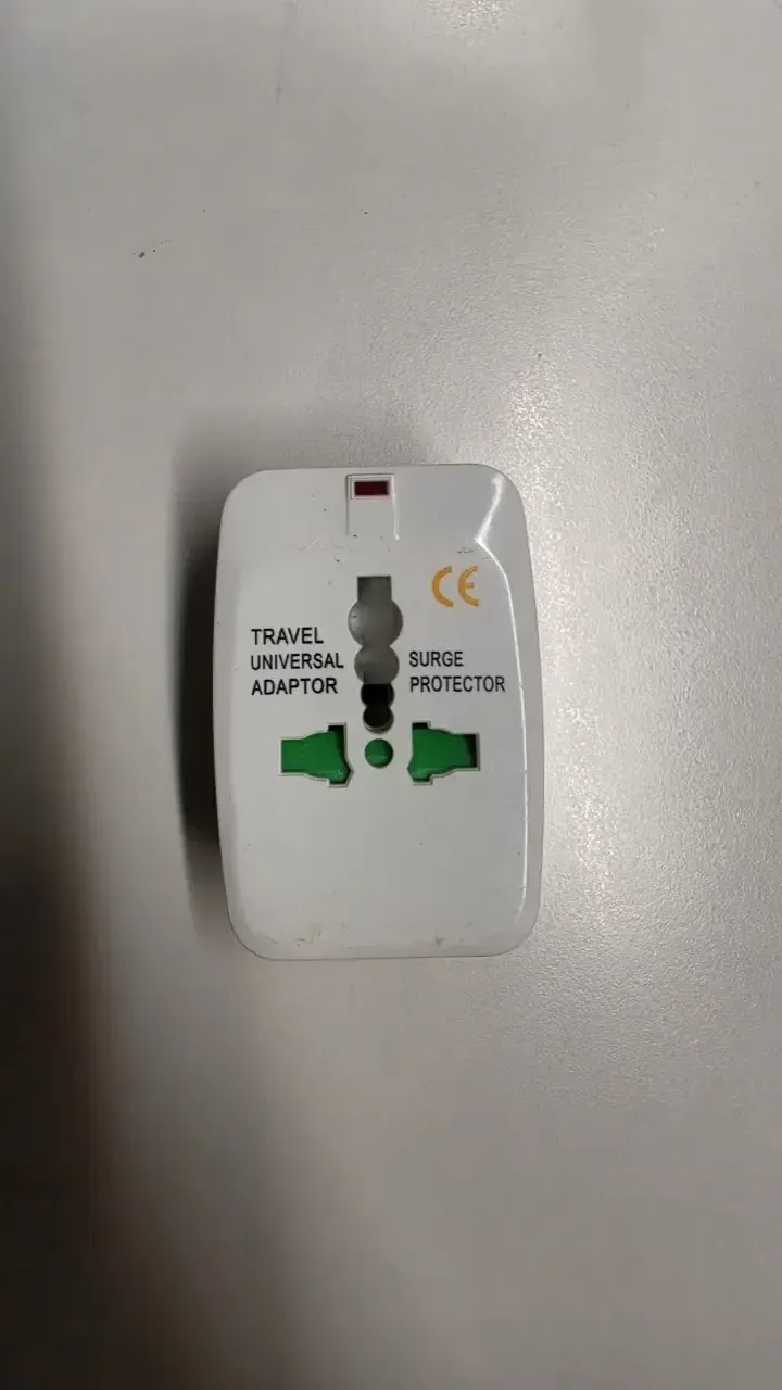 Top view of a white universal travel adapter labelled TRAVEL UNIVERSAL ADAPTOR and SURGE PROTECTOR