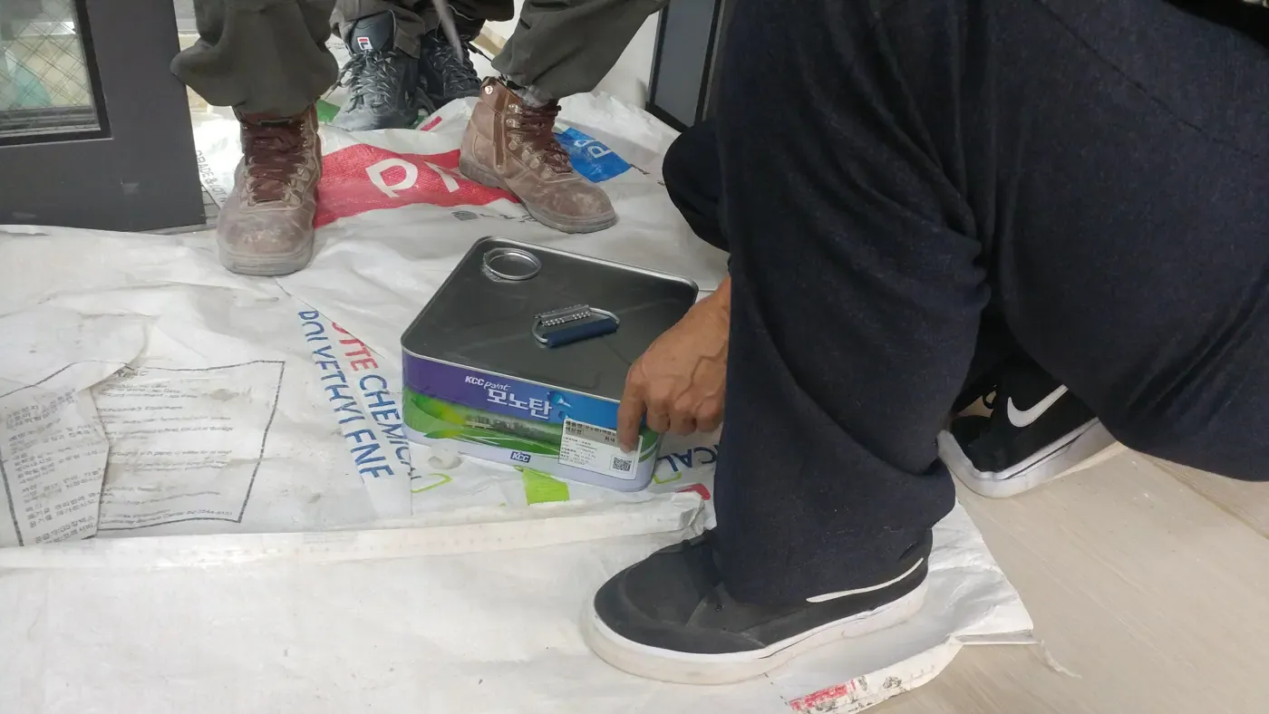 Workers kneeling on protective sheeting beside a tin of urethane waterproofing paint