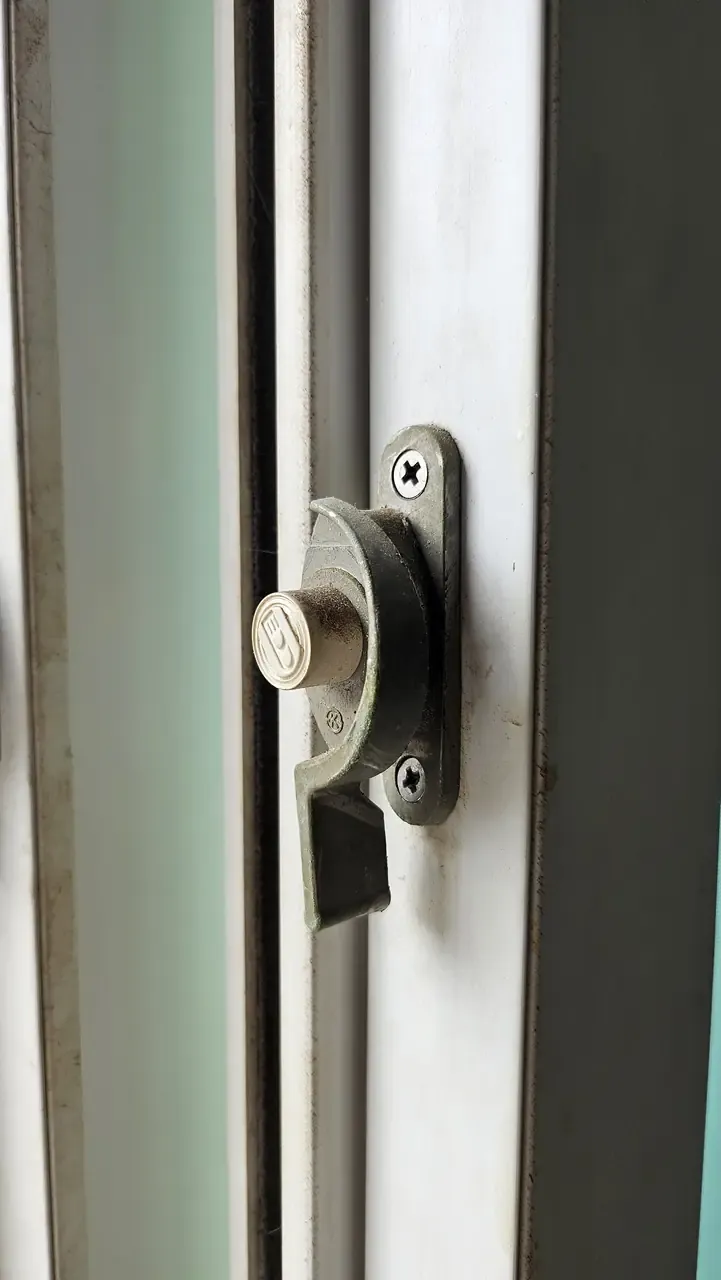 Close-up of a window's crescent latch on a white frame, screws and catch visible