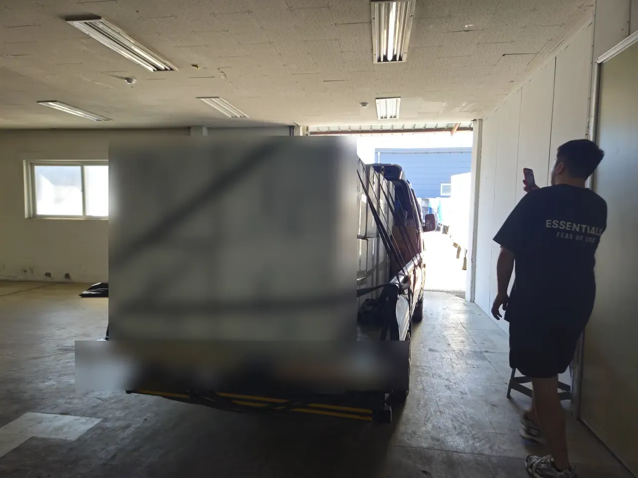 The rear of a loaded 1-ton truck inside a warehouse, boxes stacked in two tiers and held by crossed black tension straps